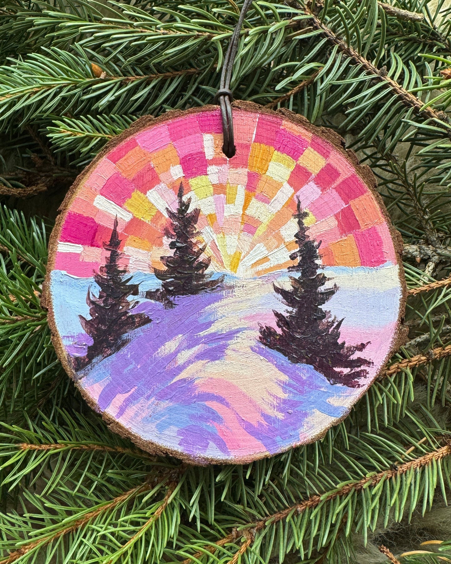 Decorative ornament with a colorful spiral design on a green pine branch.