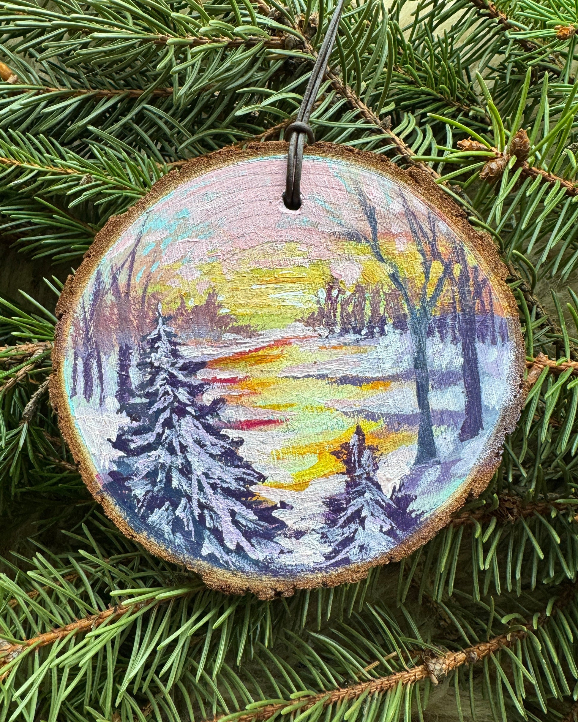 Wooden ornament with a painted design of a snowy landscape and bird, hanging on a tree.