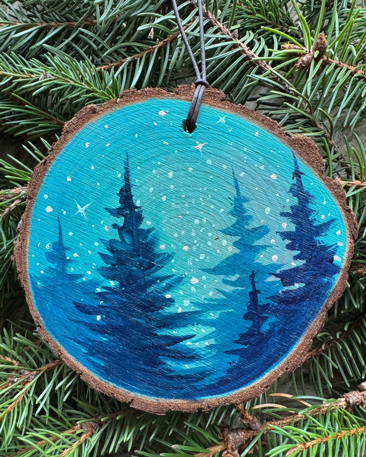 Wooden ornament with blue and black tree design on green pine branches