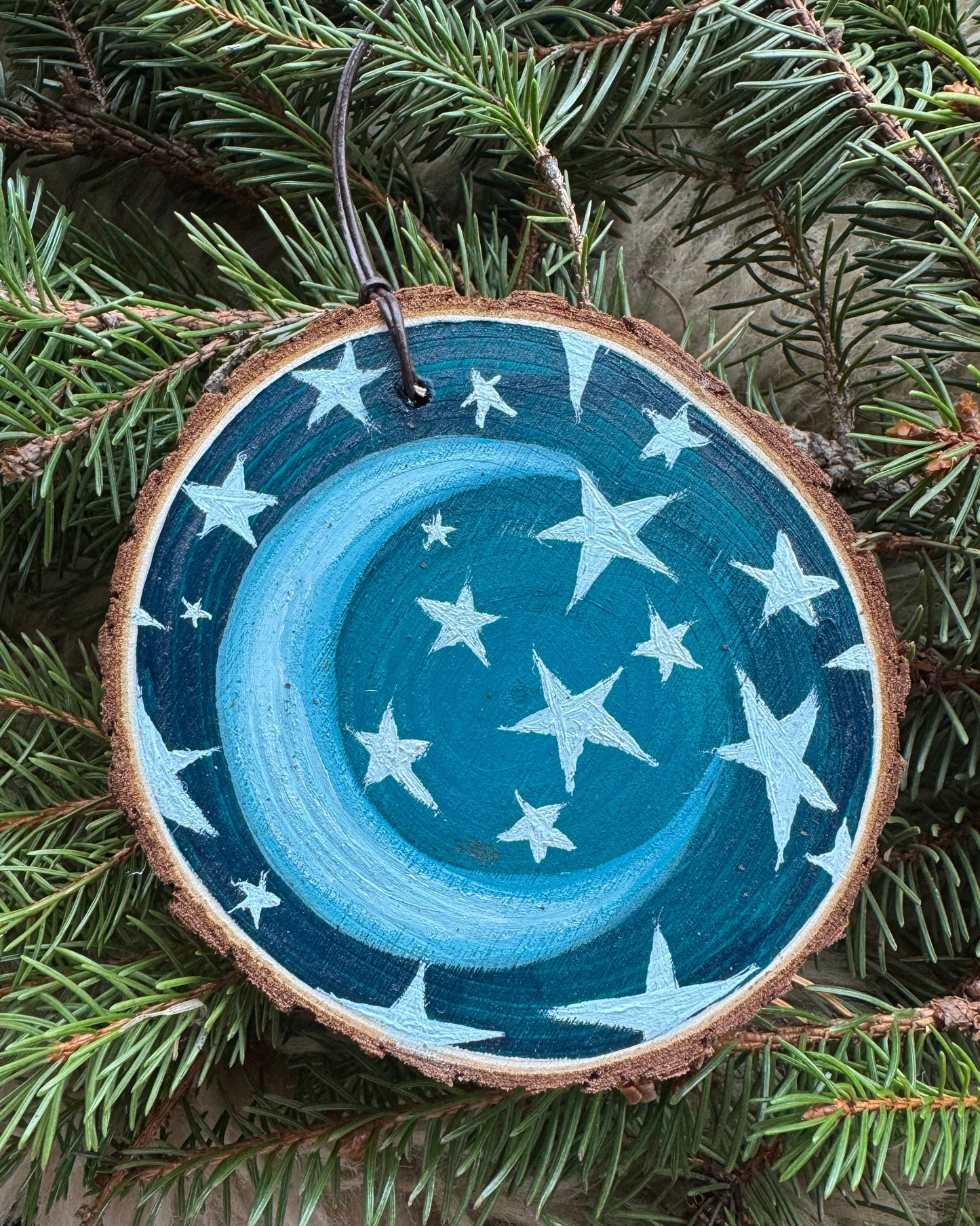 Wooden ornament with blue design and stars on a green pine branch