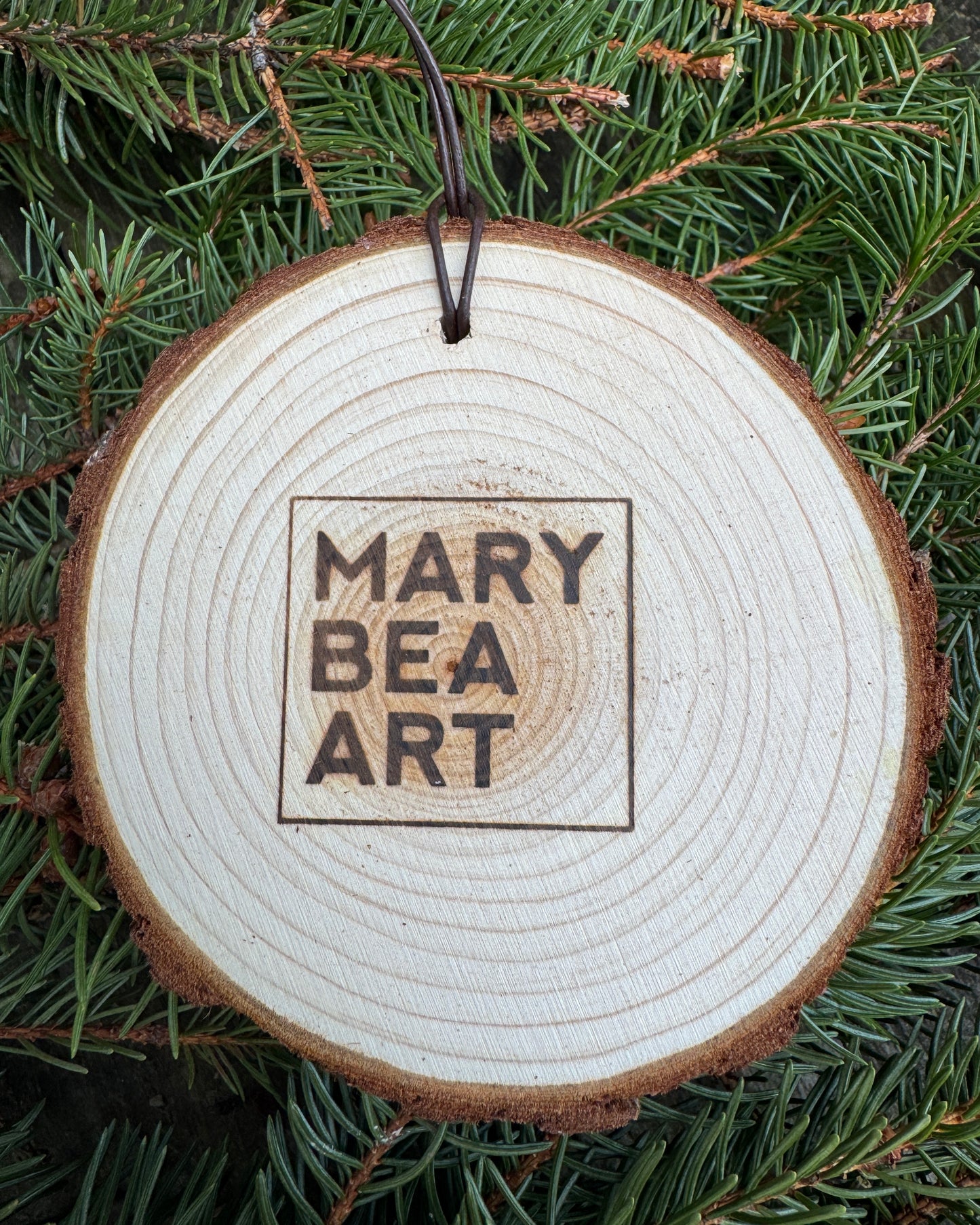 Wooden ornament with 'MARY BEA ART' engraving on a green leaf background